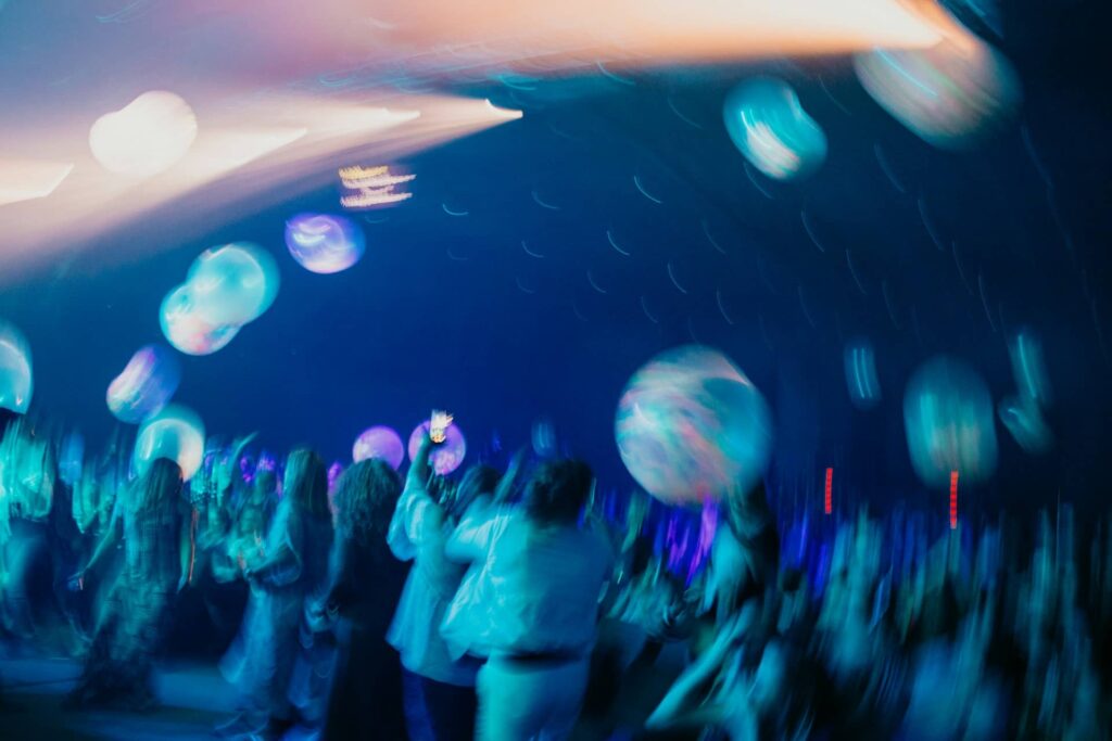 Folla che balla sotto luci blu e neon, illustrando l’atmosfera immersiva che amplifica l’impatto degli schermi digitali nei locali notturni